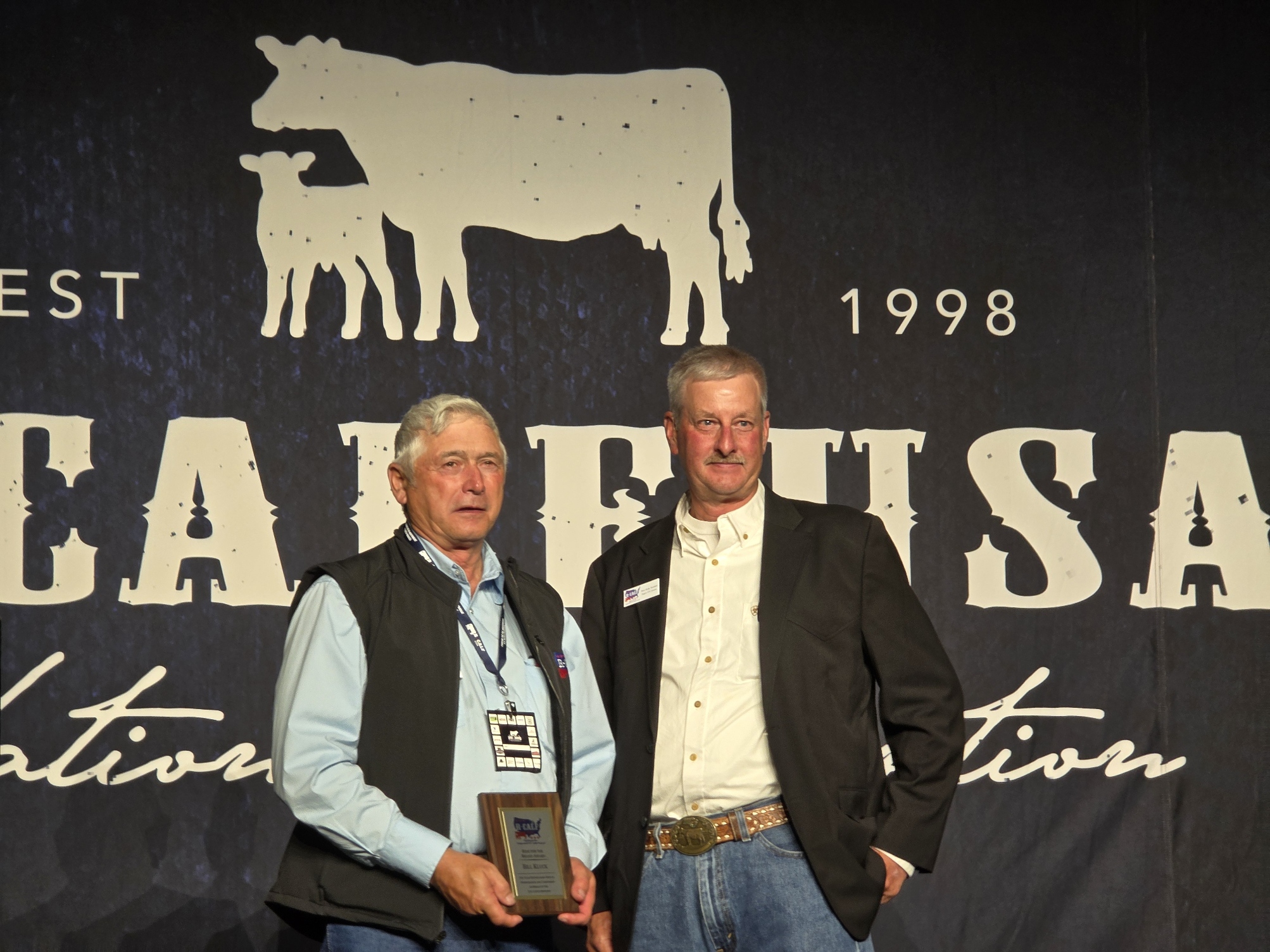 South Dakota rancher Bill Kluck receiving R-CALF USA's Riding for the Brand award on stage in front of the R-CALF backdrop.